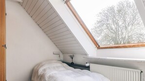 A small, sloped-roofed room with a bed, a radiator, and a window overlooking trees. - 4 Star Holiday Home in Aabybro (Aabybro)