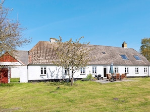 Une maison blanche à deux étages, avec un toit en tuiles, un petit jardin et un coin barbecue.