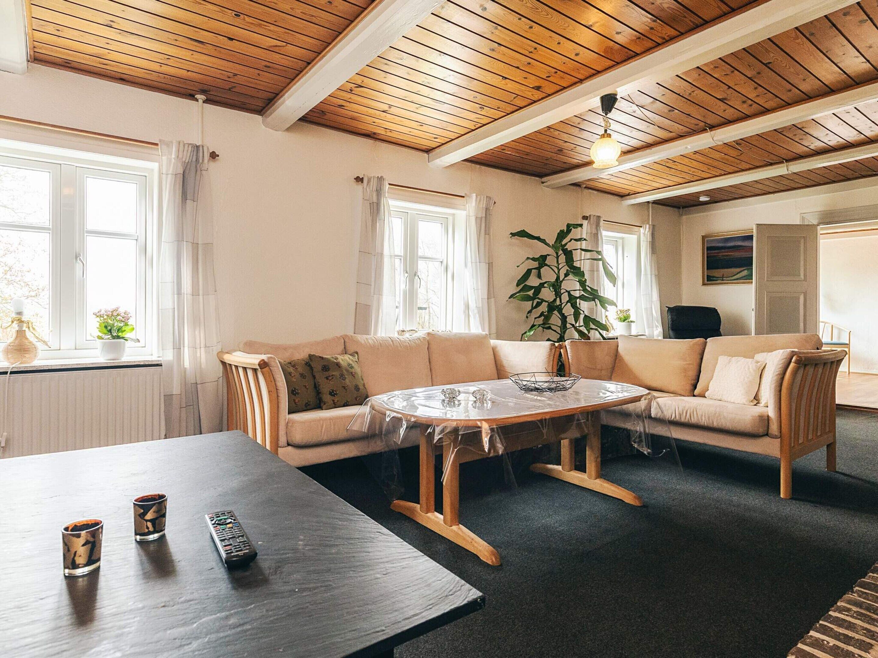A room with a wooden ceiling, a beige sofa, a round table, and a large window.
