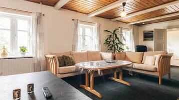 A room with a wooden ceiling, a beige sofa, a round table, and a large window.