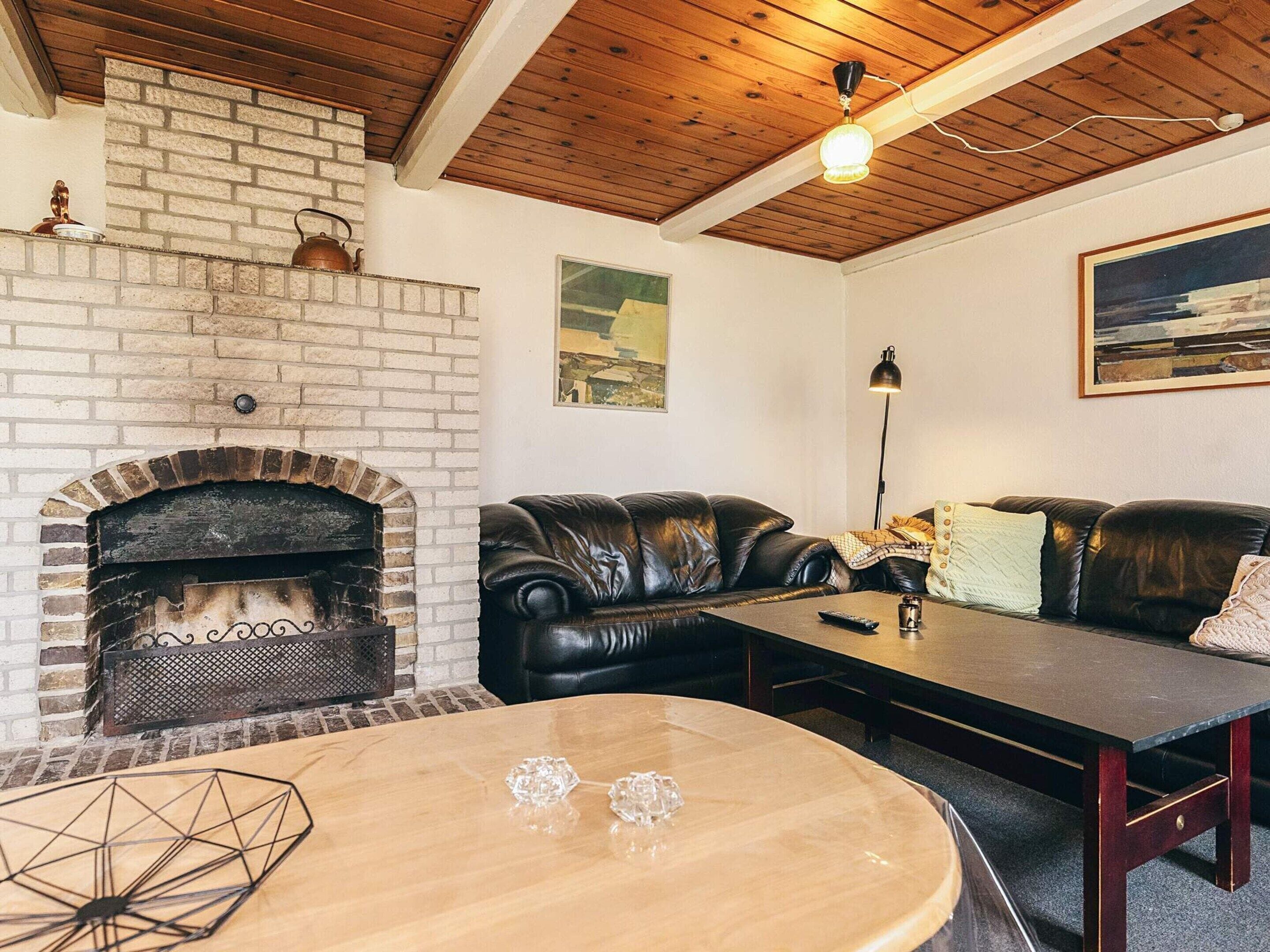 Un salón acogedor con una chimenea de ladrillo, sofás de cuero, una mesa de centro de madera y un cuadro en la pared.