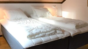 Cama doble con ropa de cama blanca en una habitación con vigas de madera en el techo y una lámpara de noche.