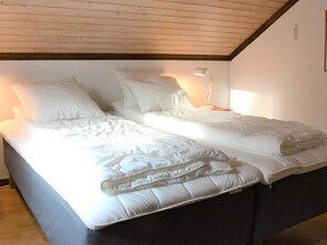 Un letto matrimoniale con biancheria bianca in una stanza con travi in legno e una lampada da comodino.