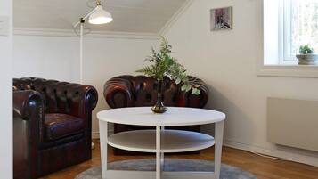 Una habitación con una mesa redonda blanca, un sofá de cuero marrón oscuro, una lámpara de pie y un ventanal.