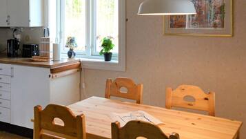 A kitchen with a wooden table and chairs, a window with plants, and a hanging light fixture.