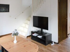 A living room with a flat-screen TV on a black stand, a wooden table with a white vase, and a staircase in the background. - 4 Star Holiday Home in Hammaro (Hammaro)