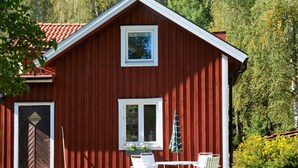 A red wooden house with a sloped roof, two windows, a door, and a small patio with a table and chairs. - 4 Star Holiday Home in Hammaro (Hammaro)