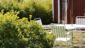 An outdoor seating area with a table and chairs, a striped umbrella, and a view of a field and trees. - 4 Star Holiday Home in Hammaro (Hammaro)