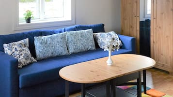 A blue sofa with patterned pillows, a white vase with flowers, and a wooden table.