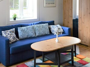 A blue sofa with patterned pillows, a white vase with flowers, and a wooden table. - 4 Star Holiday Home in Hammaro (Hammaro)