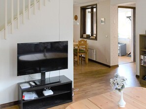 A living room with a flat-screen TV on a stand, a wooden dining table, and a white vase with flowers. - 4 Star Holiday Home in Hammaro (Hammaro)