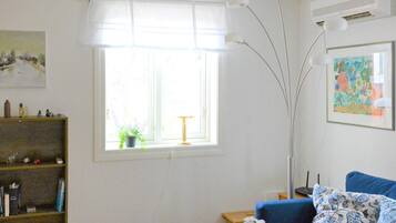 A room with a blue sofa, a bookshelf, a window with a plant, and a painting on the wall.