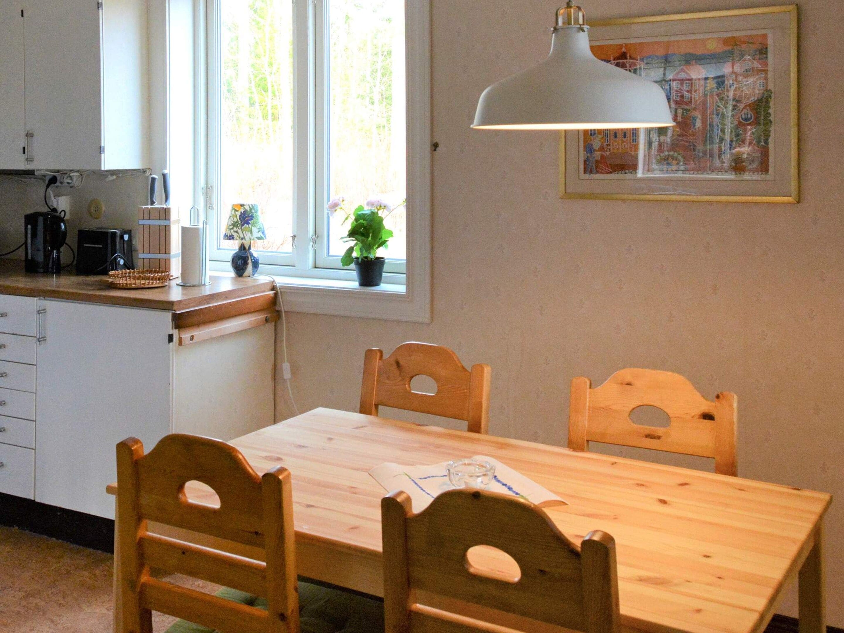 A kitchen with a wooden table and chairs, a window with plants, and a hanging light fixture.