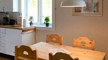 A kitchen with a wooden table and chairs, a window with plants, and a hanging light fixture.