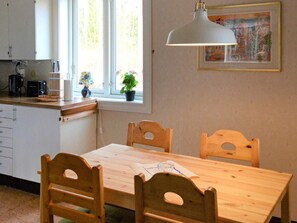 Une cuisine avec une table et des chaises en bois, une fenêtre ornée de plantes et un luminaire suspendu.