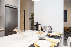 A modern kitchen with a Bosch refrigerator, a coffee maker, and a dining table set with plates and cutlery. - Alterra Vita Thessaloniki Apartment (Thessaloniki)