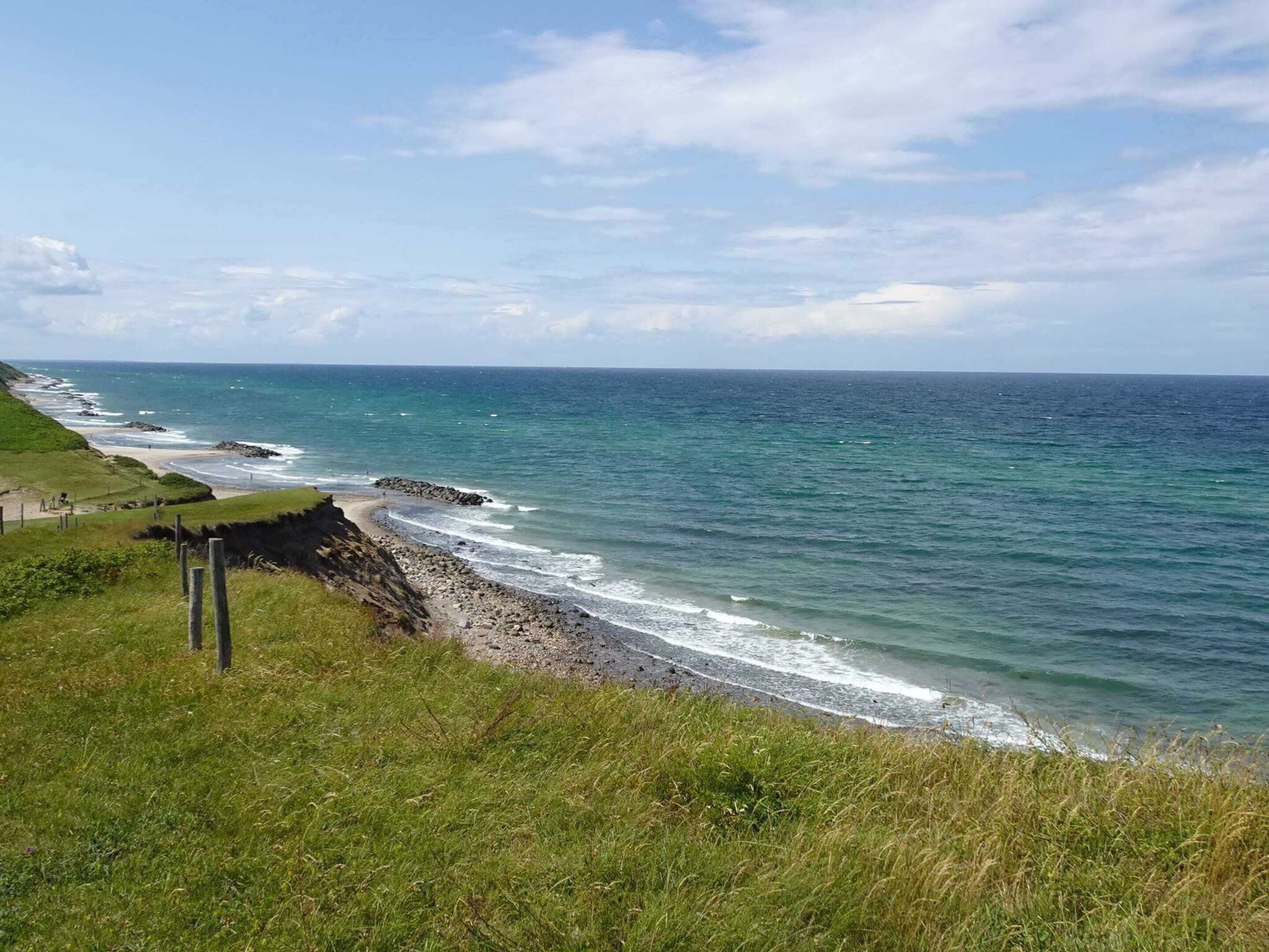 Ett kustlandskap med ett gräsområde, en stenig strand och havet.