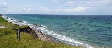 Ett kustlandskap med ett gräsområde, en stenig strand och havet.