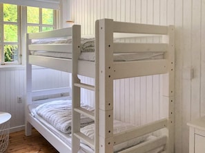 A bunk bed with white bedding, a window with a view of greenery, and a white wall.