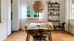 Un'area pranzo con un tavolo di legno, sedie, una lampada a sospensione, una libreria e una finestra con vista su piante.