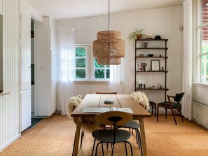 A dining area with a wooden table, chairs, a hanging light fixture, a bookshelf, and a window with a view of greenery. - 4 Star Holiday Home in Vejby (Vejby)