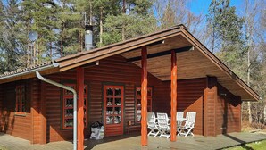 A wooden cabin with a porch, a chimney, and a small deck with chairs. - 6 Person Holiday Home in Hadsund (Hadsund)