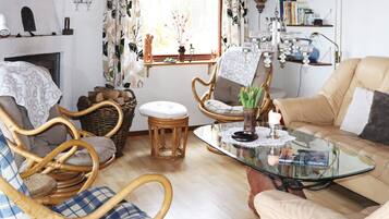 A cozy living room with wicker furniture, a glass coffee table, and a bookshelf.