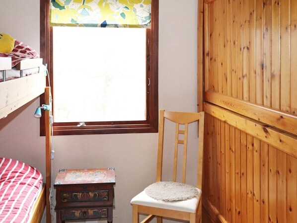 A room with a bunk bed, a small wooden chair, a window with a view, and a wooden wardrobe.