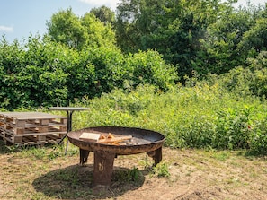 An outdoor fire pit with a table and benches, surrounded by dense greenery. - 5 Person Holiday Home in Knebel (Knebel)