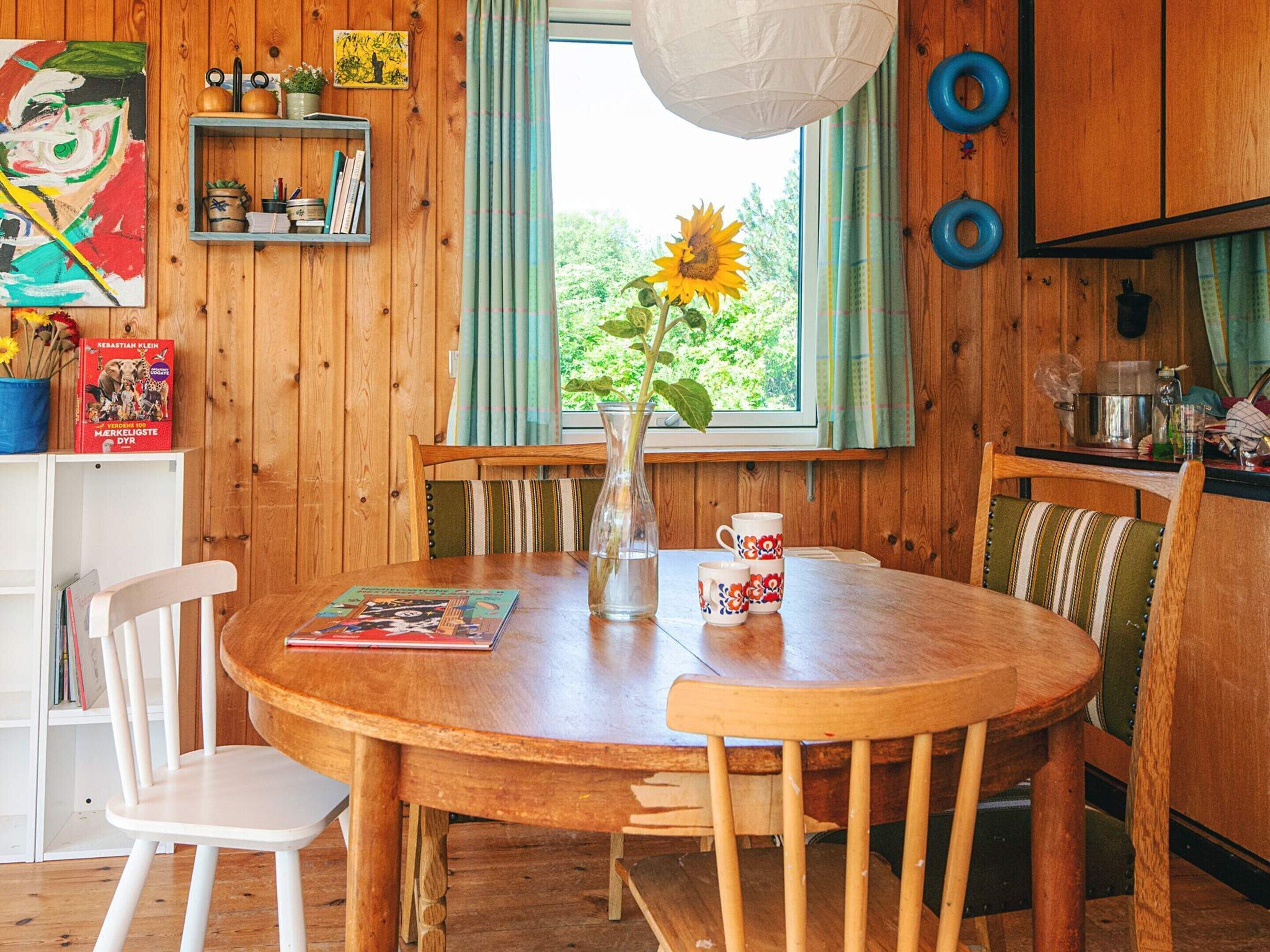 A wooden dining table with chairs, a vase with a sunflower, and a window with curtains.