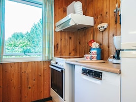 Una cocina con paredes de madera, una ventana con cortinas, una estufa, un lavavajillas y una cafetera.