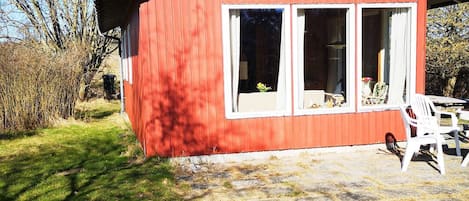 A red building with large windows, a patio with chairs, and a grassy area.