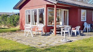 Een rood houten gebouw met een overdekte patio, compleet met een tafel en meerdere witte plastic stoelen.