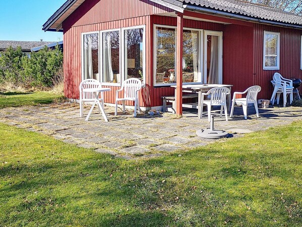 A red wooden building with a covered patio area, featuring a table and multiple white plastic chairs. - 5 Person Holiday Home in Knebel (Knebel)