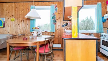 Un interior de madera con una mesa de comedor, sillas, una zona de cocina y una ventana con cortinas.