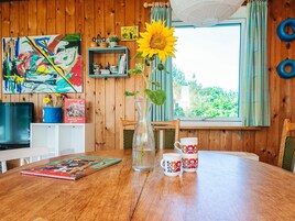 A wooden interior with a dining table, a vase with a sunflower, a mug, and a colorful painting.