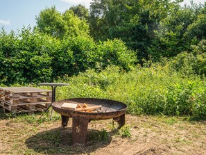 An outdoor fire pit with a table and benches in a garden setting.
