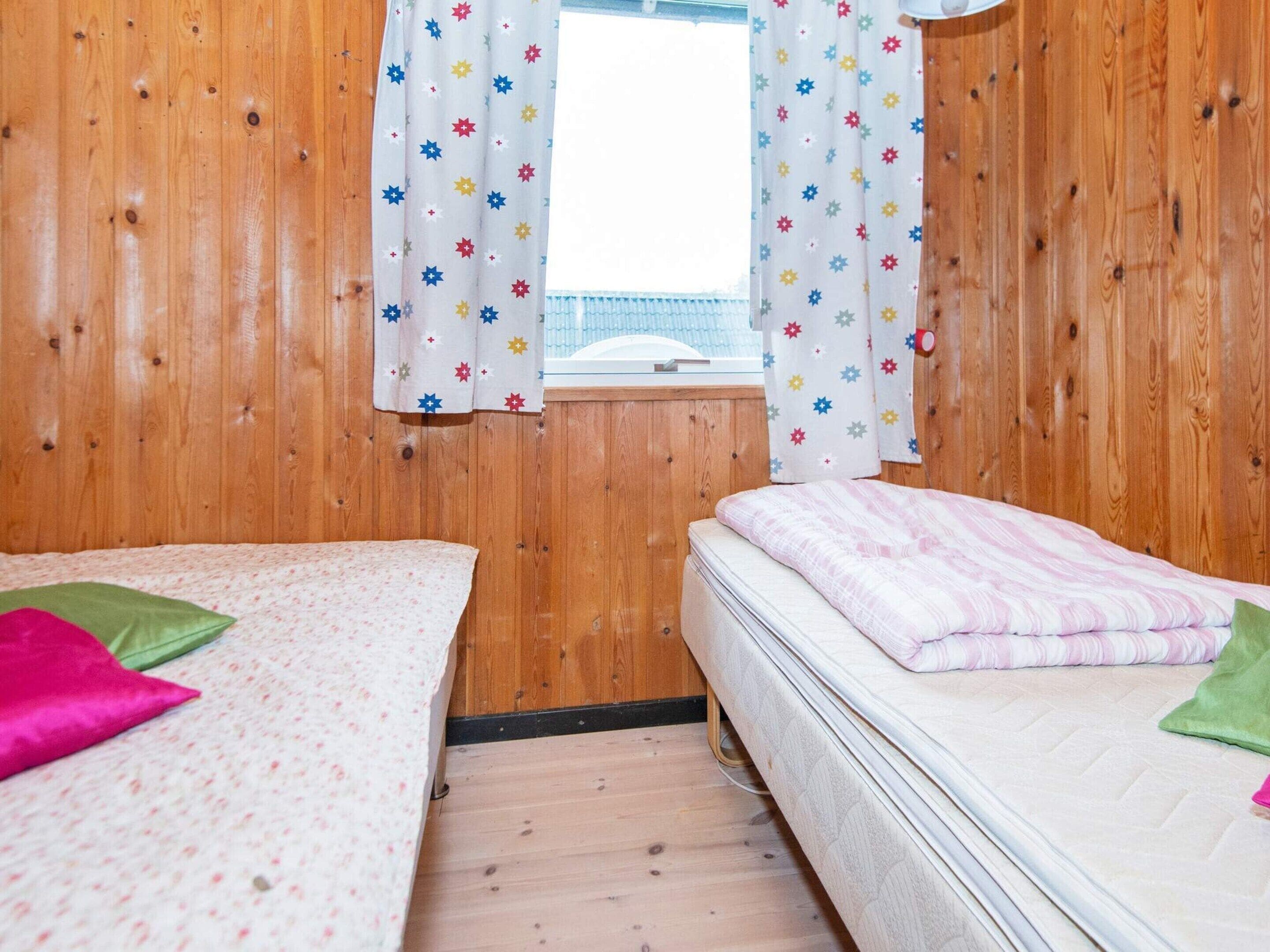 A room with two beds, wooden walls, a window with star-patterned curtains, and a view of a building outside.