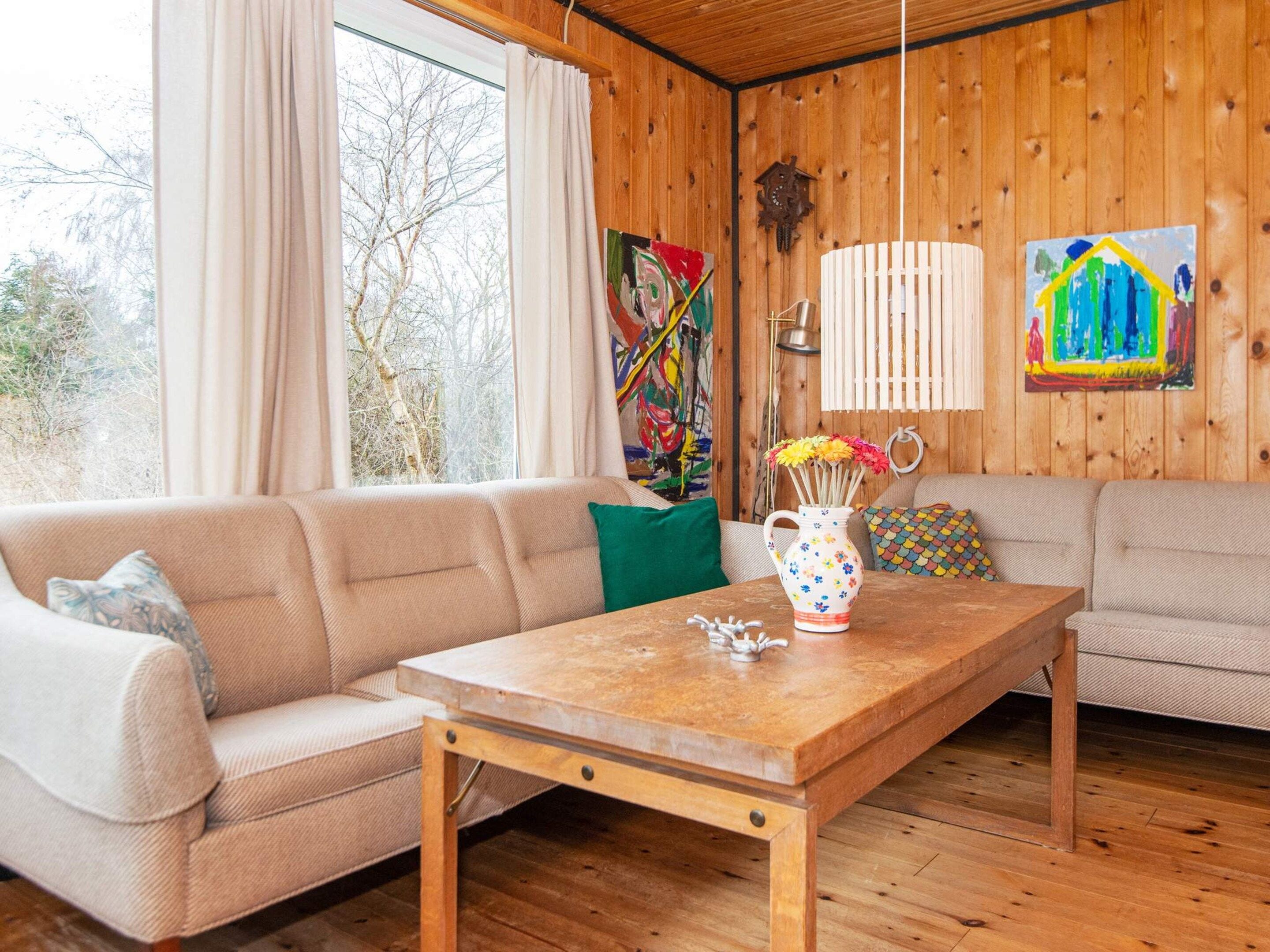 A cozy living room with a wooden floor, a beige sofa, a wooden coffee table, and a window with curtains.