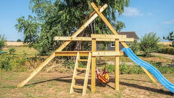 A wooden swing set with a slide in a grassy outdoor area.