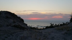 Una playa con vista al atardecer, terreno arenoso y vegetación.