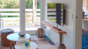 Ein modernes Wohnzimmer mit an der Wand montiertem Fernseher, einem Holztisch, zwei Stühlen und Blick ins Freie durch große Glasüren.