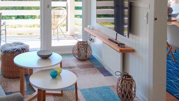 Una sala de estar moderna con un televisor montado en la pared, una mesa de madera, un sillón de mimbre y vistas al exterior.