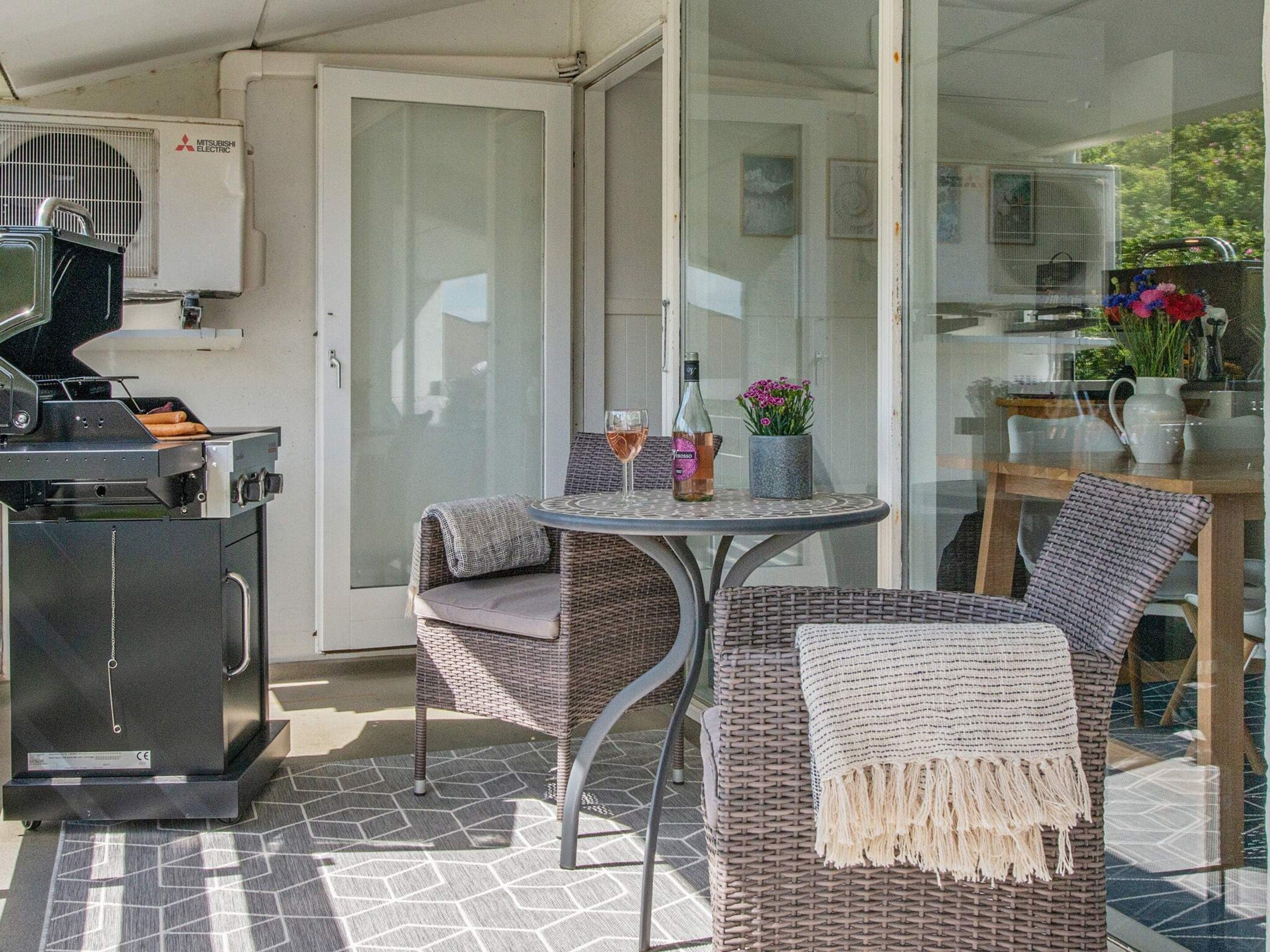 An outdoor patio with a grill, wicker furniture, and a table with drinks.