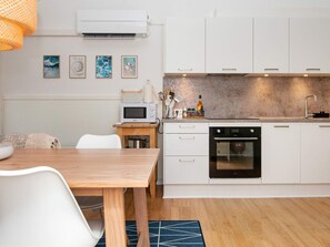 A compact kitchen with white cabinetry, a microwave, a stove, and a sink. There are framed pictures on the wall and a small wooden table with chairs.