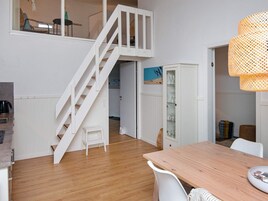 Un interior moderno con una escalera de madera, una zona de comedor con una mesa y un mueble con puertas de vidrio.