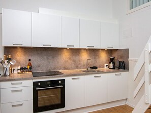 Una cocina moderna con alacenas blancas, horno empotrado, pileta y cafetera.