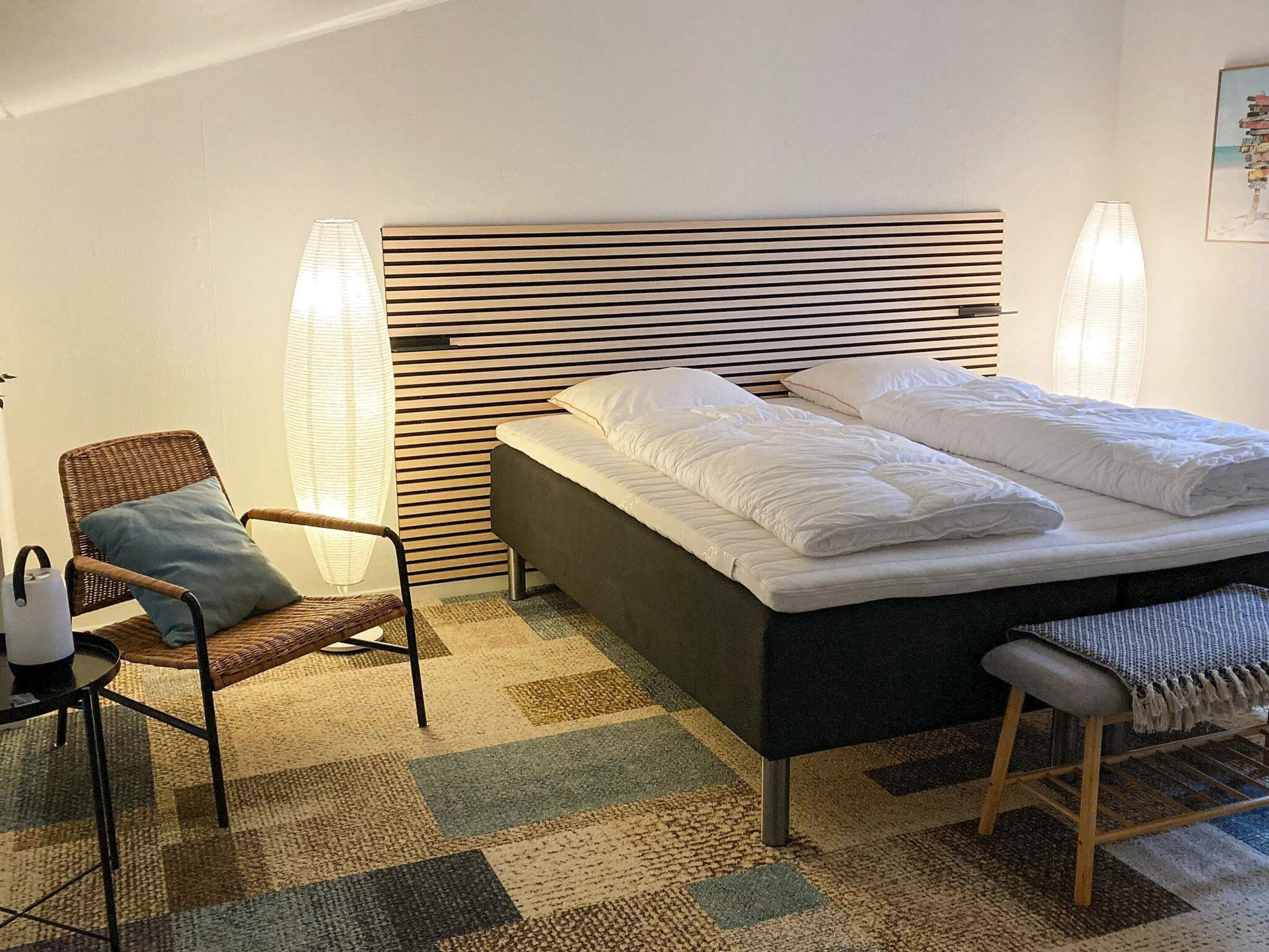 Une chambre à coucher comprenant un lit, une chaise, une table de chevet et une lampe fixée au mur.