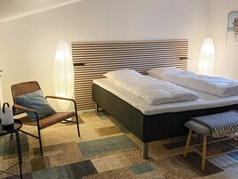 Un dormitorio con cama, una silla, una mesita de noche y una lámpara de pared.