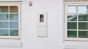 A building facade with two windows, a small wall-mounted light, and a security camera. - 5 Star Holiday Home in Lokken (Lokken)